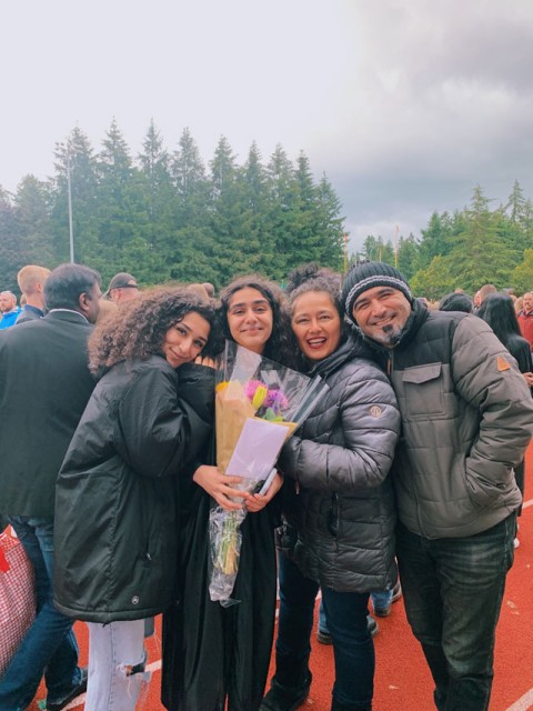 a family of 4 standing in front of trees wearing warm jackets