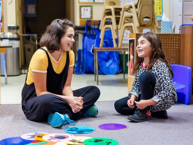 teaching assistant sitting on floor with child and a game